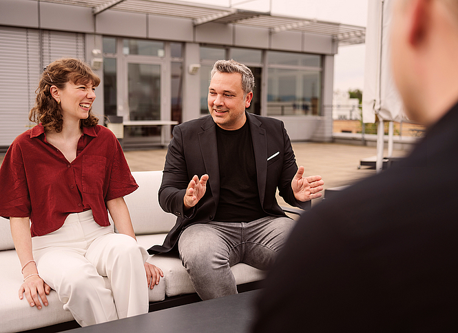 Drei Kolleginnen und Kollegen unterhalten sich auf der Dachterrasse. 