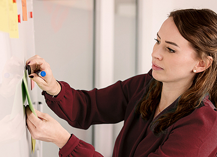 Eine Mitarbeiterin steht am Whiteboard und schreibt etwas auf.